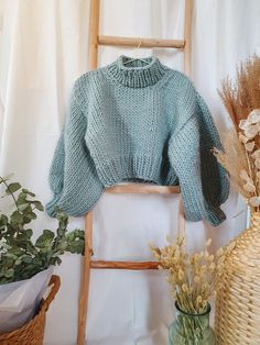 a blue sweater sitting on top of a wooden ladder next to a vase with flowers