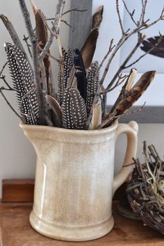 a white pitcher filled with feathers on top of a wooden table