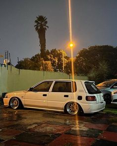 two white cars parked next to each other in front of a green wall and palm trees