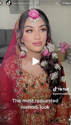 a woman wearing a red and gold bridal outfit with flowers in her hair, looking at the camera