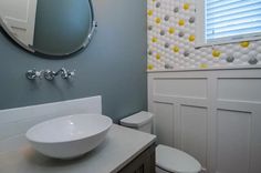 a white bowl sink sitting next to a toilet in a bathroom under a round mirror