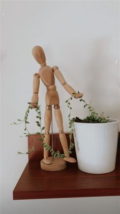 a wooden mannequin standing next to a potted plant on top of a table