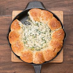 a pan filled with bread and spinach on top of a wooden cutting board