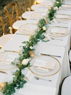 the table is set with white and gold plates, silverware, greenery and candles