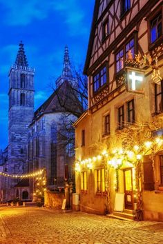 a cobblestone street lined with tall buildings and lit up christmas lights at night