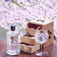 a bottle of gin next to a wine glass on a table with cherry blossoms in the background