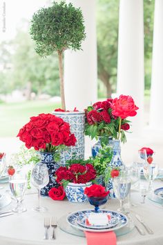 red roses in blue and white vases sit on a table with plates, utensils and silverware