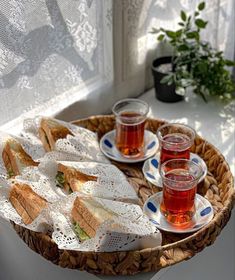 sandwiches and tea on a wicker tray in front of a window