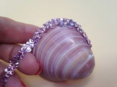 a hand holding a pink seashell with lots of crystals