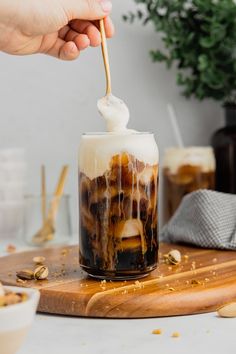 someone is dipping something into a glass with ice cream and caramel in it on a cutting board