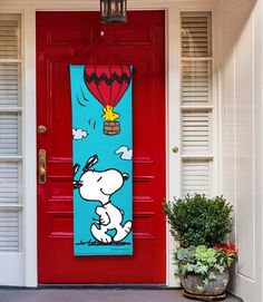 a red door with a snoopy banner hanging from it's side and potted plants in front