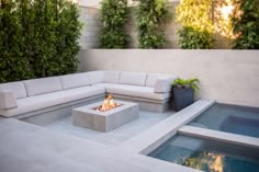 an outdoor fire pit in the middle of a patio with white furniture and greenery