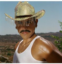 a man wearing a straw hat with chains around his neck and mustache, in the desert