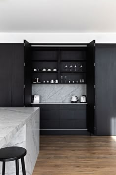 a kitchen with black cabinets and marble counter tops, along with stools in front of it