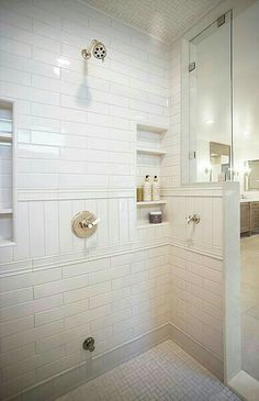 a white tiled bathroom with glass shower doors and shelves on the wall, along with a walk in shower