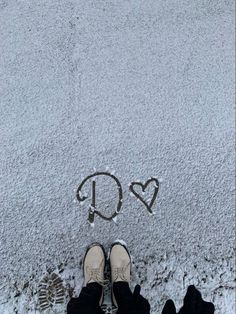 someone's feet standing in the snow with an arrow and heart drawn on it