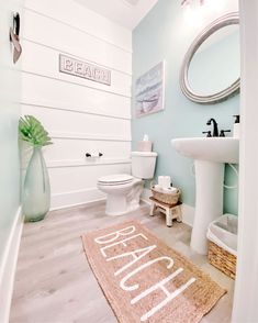 a bathroom with blue walls and white fixtures, including a rug that says beach on the floor