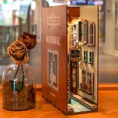 a fake rose in a glass vase sitting next to a cardboard box on a table