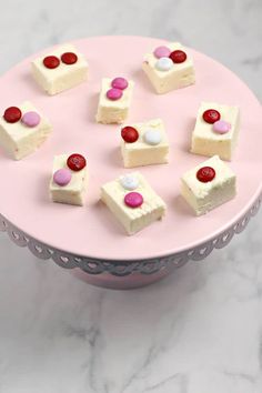 small pieces of cake on a pink plate with white frosting and red candies