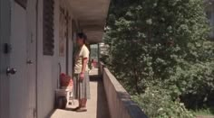 a woman standing on the side of a building next to a tree filled sidewalk with luggage