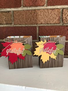 two small bags with fall leaves on them are sitting on a white table next to a brick wall