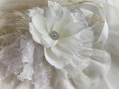 a white flower is sitting on top of some lacy fabric and laces, with a beaded brooch in the center