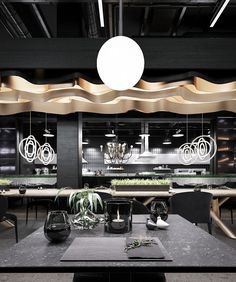 an indoor dining area with black tables, chairs and hanging plants in the center of the room