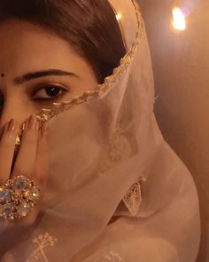 a woman wearing a veil covering her face and holding her hands to her face, with lights in the background