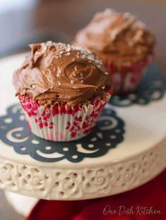 two cupcakes with chocolate frosting on a cake stand