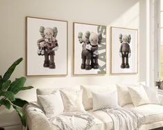 three framed pictures hang on the wall above a couch in a living room with white furniture