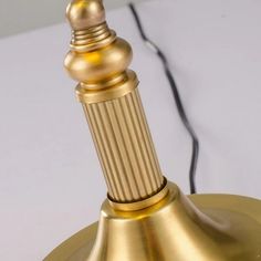 a close up of a golden lamp on a white surface with wires in the background