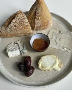 an assortment of cheeses and bread on a plate with jam in a small bowl