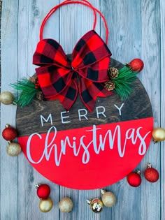 a wooden sign that says merry christmas with ornaments around it and a bow on top