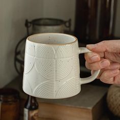 a person holding a white coffee mug in their hand next to a stack of books