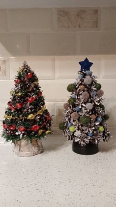 two small christmas trees sitting on top of a counter next to each other in front of a white tiled wall