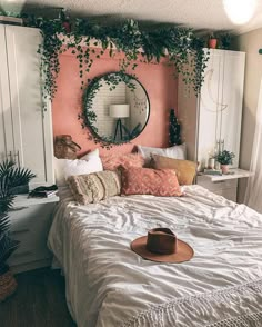 a bedroom with pink walls, white bedding and plants on the headboard is decorated with greenery