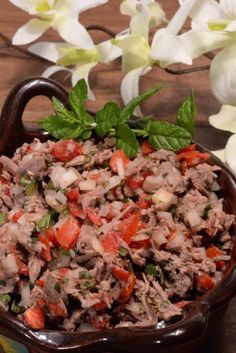 a bowl filled with meat and veggies on top of a wooden table next to flowers