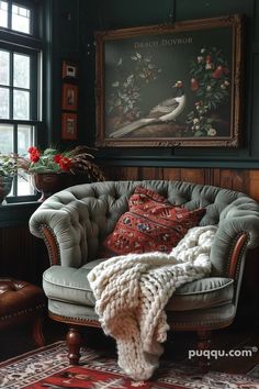 a chair with a blanket on it in front of a window and a large painting