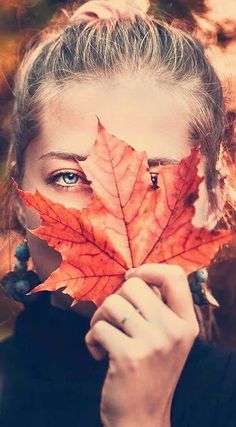 a woman holding up a leaf to her face with the leaves in front of her face