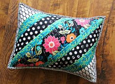 a black and white pillow with colorful flowers on it sitting on a wood floor next to a wooden table