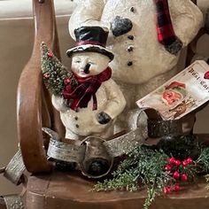 a snowman sitting on top of a wooden chair next to a snow man holding a book