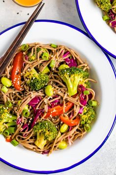 two plates with noodles, broccoli and carrots on them next to orange juice