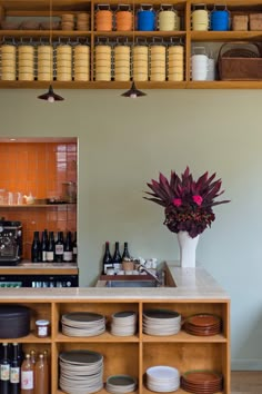 a counter with plates and bowls on it in a room that has shelves filled with wine bottles