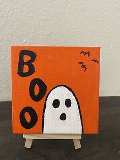 an orange and black painting with a ghost on it's face is sitting on a small easel