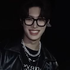 a young man wearing glasses and a leather jacket smiles at the camera while standing in front of a black background