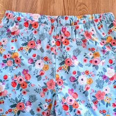 a pair of blue floral shorts with pink and red flowers on them sitting on a wooden floor