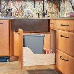 a kitchen with wooden cabinets and an open trash can in the middle of the cabinet