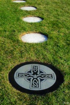 a black and white cross is in the middle of some stepping stones on green grass