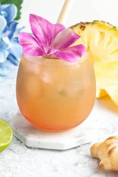 a drink in a glass with a pink flower on the rim next to sliced pineapples