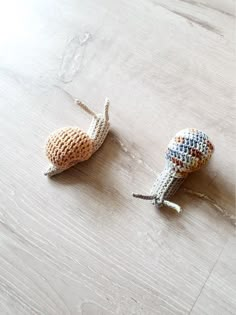 two crocheted snails sitting on top of a wooden table next to each other